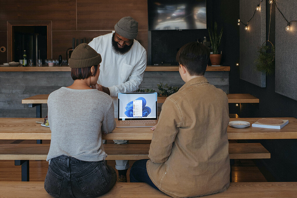 Two people working on a computer in a coffeeshop while a barista pours their coffee